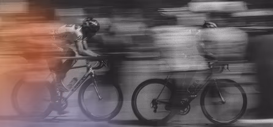 Two cyclists racing fast, captured with motion blur creating streaks of color and movement.